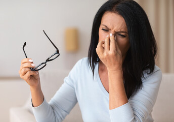 Tired mature woman massaging nosebridge at home