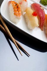 Sushi served on a white plate with chopsticks. Studio photo isolated on grey background. Selective focus on object. Bright light setting.