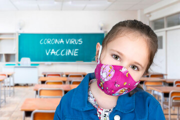 Girl in a classroom wearing a face mask and the words corona virus vaccine written on a blackboard.
