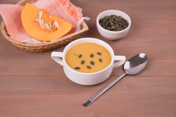 White plate with pumpkin puree Soup, a piece of pumpkin and pumpkin seeds on a wooden background. Horizontal orientation