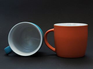 Simple two beautiful orange and blue cups with a handle without a pattern on a dark background