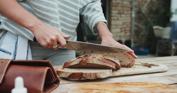 Woman chef cooking tasty and healthy delicious food outdoor. Female hand cuts pieces of raw bread by professional sharp knife on a wooden table at the summer kitchen.Cooking food professional for vlog