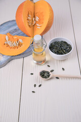 Pumpkin oil in a glass bottle, pumpkin and pumpkin seeds on a light table.Alternative to traditional oil. Close up