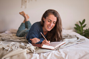 Woman lying on her bed writing in her journal