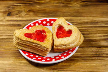 Heart shaped puff cookies with jam on a wooden table. Dessert on Valentine`s Day