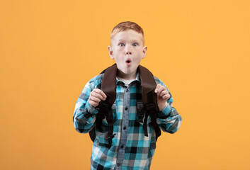 Amazed redhead schoolboy with backpack over yellow studio background