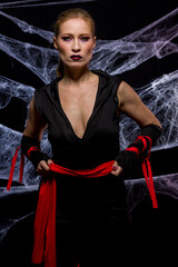 Woman dressed in elegant way as witch for Halloween party with black background and spider webs