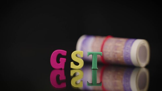 Currency note bundle falling on GST wooden letters, concept of Fall in Goods and service tax collection
