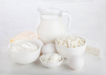 Fresh dairy products on white table background. Glass jar of milk, bowl of sour cream and cottage cheese and mozzarella. Eggs in and cheese.