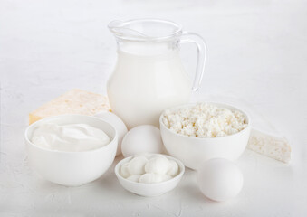 Obraz na płótnie Canvas Fresh dairy products on white table background. Glass jar of milk, bowl of sour cream and cottage cheese and mozzarella. Eggs in and cheese.