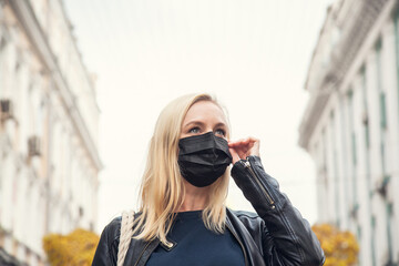 Fototapeta premium Woman in the background of the city wants to remove a black protective face mask
