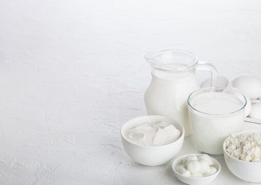 Fresh dairy products on white table background. Jar and glass of milk, bowl of sour cream, cottage cheese and mozzarella. Eggs in wooden box. Space for text