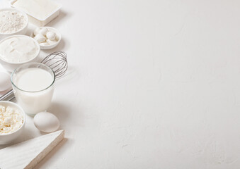 Obraz na płótnie Canvas Fresh dairy products on white table background. Glass of milk, bowl of flour, sour cream and cottage cheese and eggs. Steel whisk. Top view. Space for text
