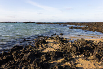 Small waves on shallow water reaching volcanic rocks beach in Lanzarote. Empty natural landscape on sunny day in Canary Islands