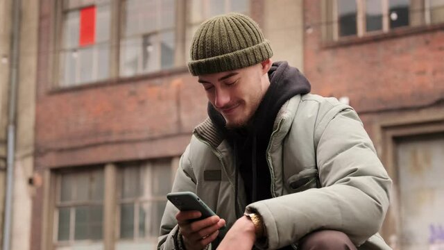 Young student hipster man using touch mobile phone outdoor on the street. Surfing social media, checking news, playing mobile games, texting message.