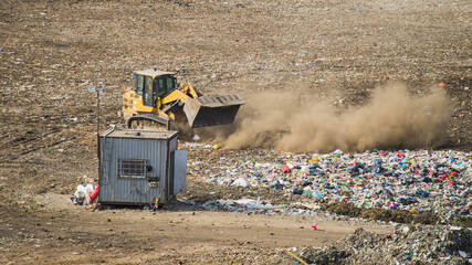 Yellow tractor unloading waste on huge landfill of big city. A lot of garbage on dumping site. Waste sorting.