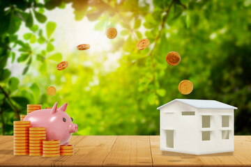 Pink piggy bank,coin dropping from top,stack gold dollar coin,on wood table,with house...