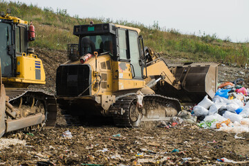 Fototapeta premium Yellow tractors. Pile of household garbage. Waste sorting and preparation for recycling on landfill. Caring for environment.