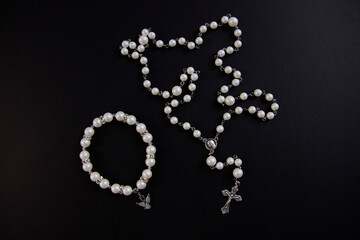 White rosary and bracelet on black background, view from above