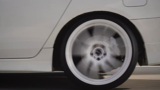 Side view of modern powerful white car rides on summer highway. Footage. Perfect auto drives fast on country road. Large sports alloy wheels with powerful brakes. Static camera, cars leave the frame.