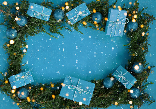 Flat lay new year Christmas blue boxes, blue balls, pine tree with lights and snow flakes on blue background. High quality photo