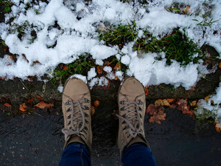 boots standing on an alley with autumn leaves covered with snow