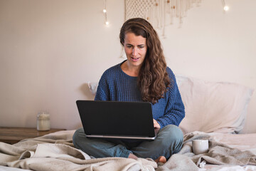 Woman in blue sweater casually working on laptop whilst sat on bed