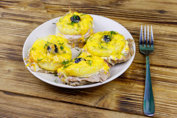 Pieces of baked pork with pineapple, cheese and olive on a wooden table