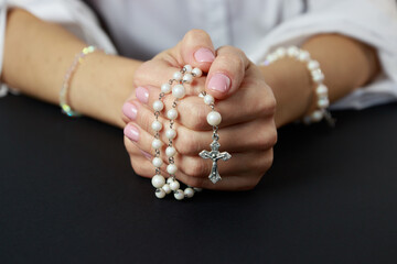 Spiritual prayer to god, with verve or rosary in the hands of a young girl. Black background. Close-up.
