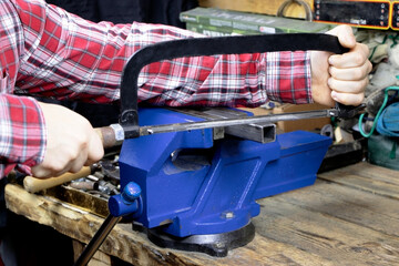 A worker is cutting by hacksaws metal profile. A handyman with hacksaws for metal. A locksmith vise