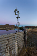 Wide angle view of a reservoir and a windpomp/windmill on a farm in the Tankwa Karoo with dusk...