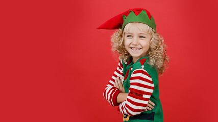 Merry Christmas Little girl in Santa elf helper costume on bright red vivid color background. Red and green. Portrait of lovely elf child. Copy space