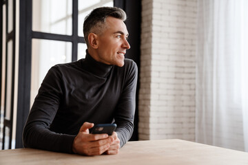 Handsome smiling man using mobile phone while sitting at home