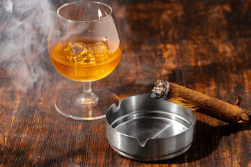 Glass of whisky and lighted cigar in an ash tray