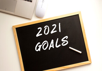 Text 2021 GOALS written in chalk on a slate board. Office desk.
