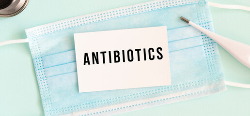 White card with the inscription ANTIBIOTICS on a medical protective mask.