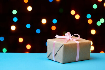 Christmas or New Year gift box on a blue surface against a background of colorful lights. Close-up, selective focus