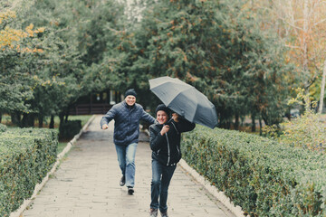 father and daughter running with umbrella, autumn city street, happy people together, parent and children