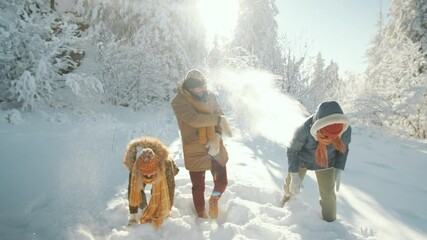Group of young excited male and female friends playing snowballs and throwing snow in forest while having fun outdoors on sunny winter day