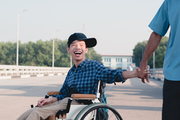 Fototapeta premium Asian special child on wheelchair wearing blue shirt and cap with backpack hold hands with father on public street, Lifestyle in the education age of disabled children, Happy disabled kid concept.