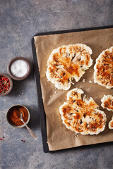 raw cauliflower steaks with spice on baking tray. plant based meat substitute