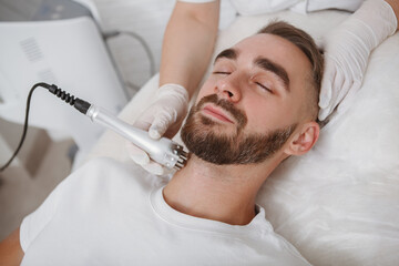 Obraz na płótnie Canvas Bearded man relaxing at beauty salon getting facial cosmetology treatment by beautician