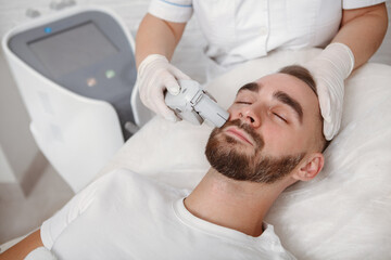 Handsome bearded man getting facial laser treatment by cosmetician