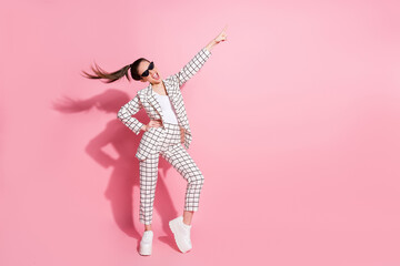 Full size photo of young happy positive smile girl wear pants point index finger empty space ad promo isolated over pink color background