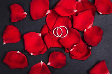 Two silver wedding rings on red rose petals