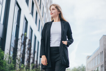 a cute blonde in a business black suit walks around the territory of a business center
