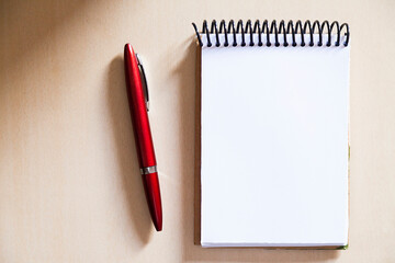 Blank notepad on the wooden table, with a red pen at the side, with sunlight hitting the side. Notepad for noting reminders. Annotation concept. Object concept. Copy space