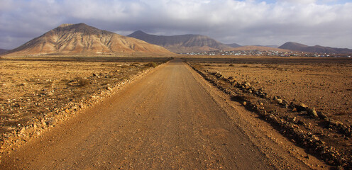Stone path with a desert landscape, with a town and mountains in the background. © Carlos Ondono