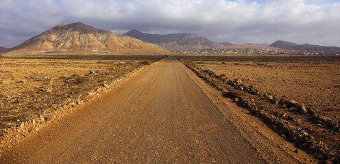 Stone path with a desert landscape, with a town and mountains in the background.