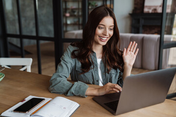 Beautiful smiling woman waving hand and working with laptop